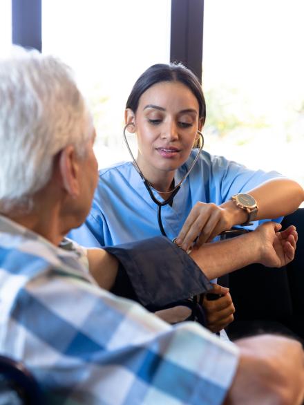 Biracial female doctor examining caucasian senior man's blood pressure with gauge and stethoscope. Home, sickness, unaltered, hypertensive, healthcare, patient, retirement, recovery, disability.